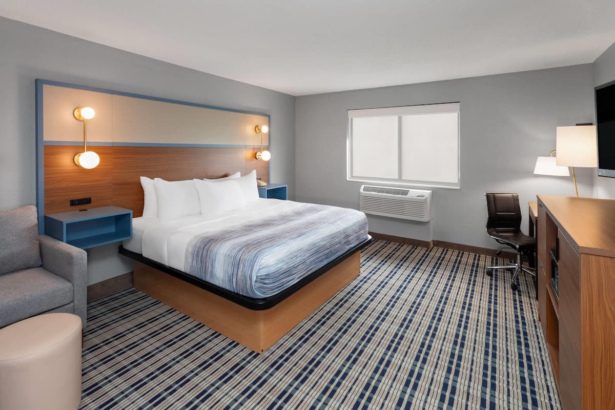 Una habitación de hotel con cama, mesitas de noche, escritorio, silla, televisor y ventana.