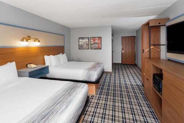 A hotel room with two beds, a TV, a wooden cabinet, and a patterned carpet.