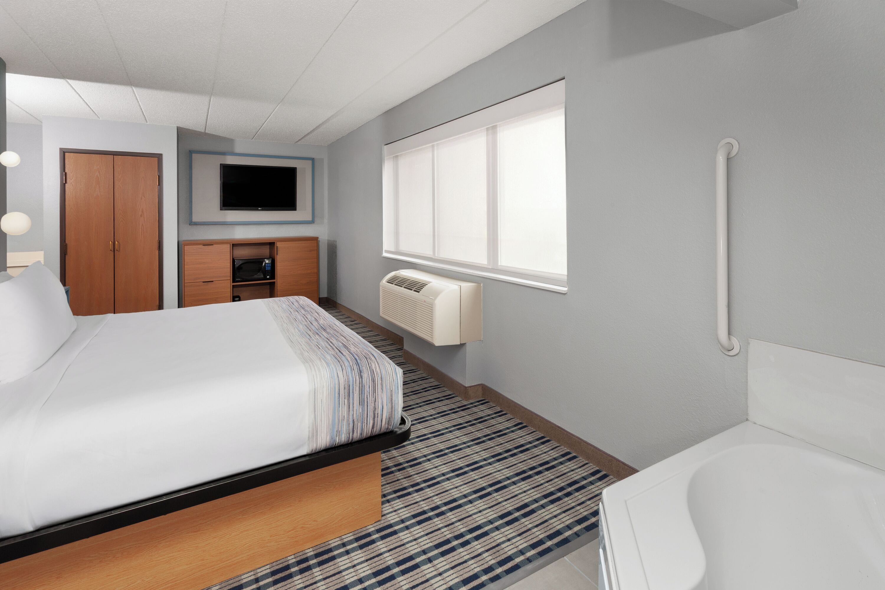 A hotel room with a bed, a TV, a window, a radiator, and a shower.