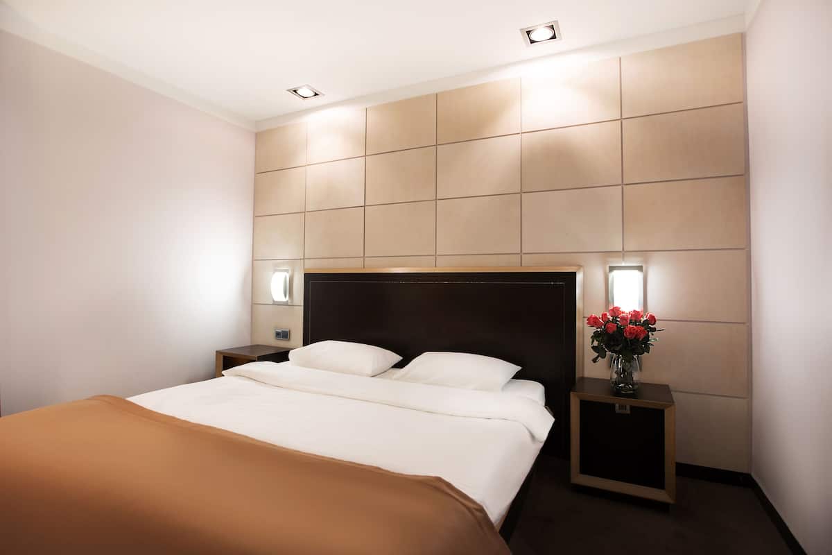 A modern hotel room with a large bed, two bedside tables, and a wall-mounted light fixture.
