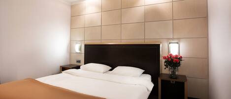 A modern hotel room with a large bed, two bedside tables, and a wall-mounted light fixture.