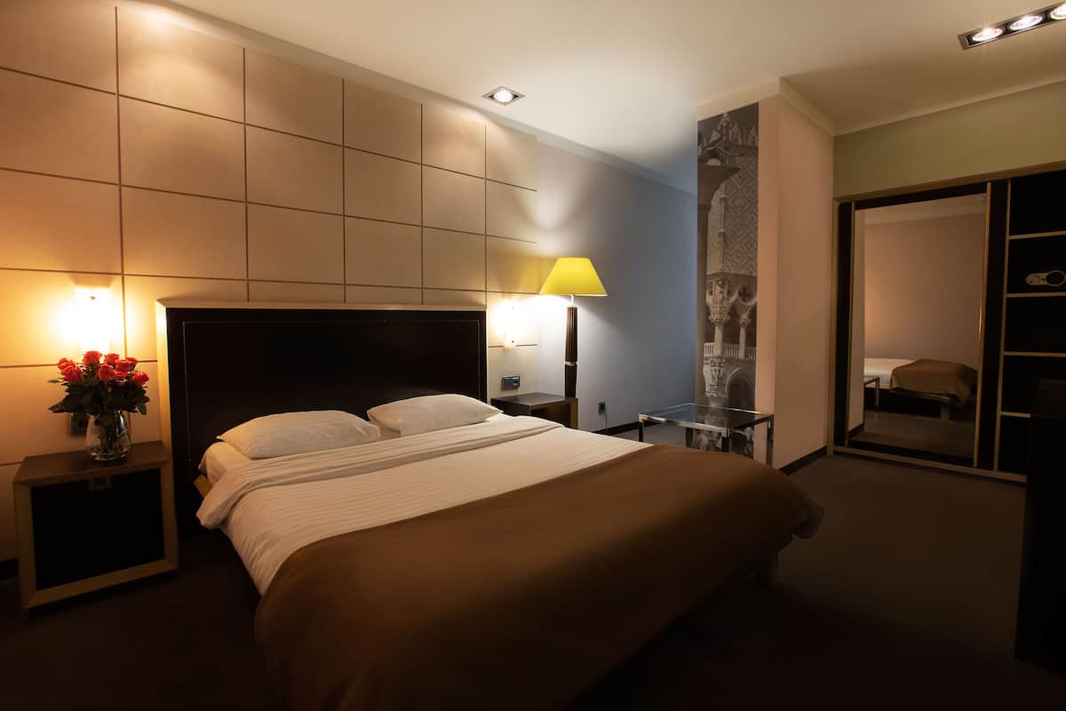 A hotel room with a large bed, bedside lamps, a nightstand with a vase of flowers, and a mirror on the wall.