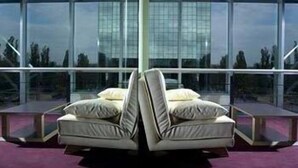 A modern room with a unique L-shaped sofa and a large window offering a view of a glass building.