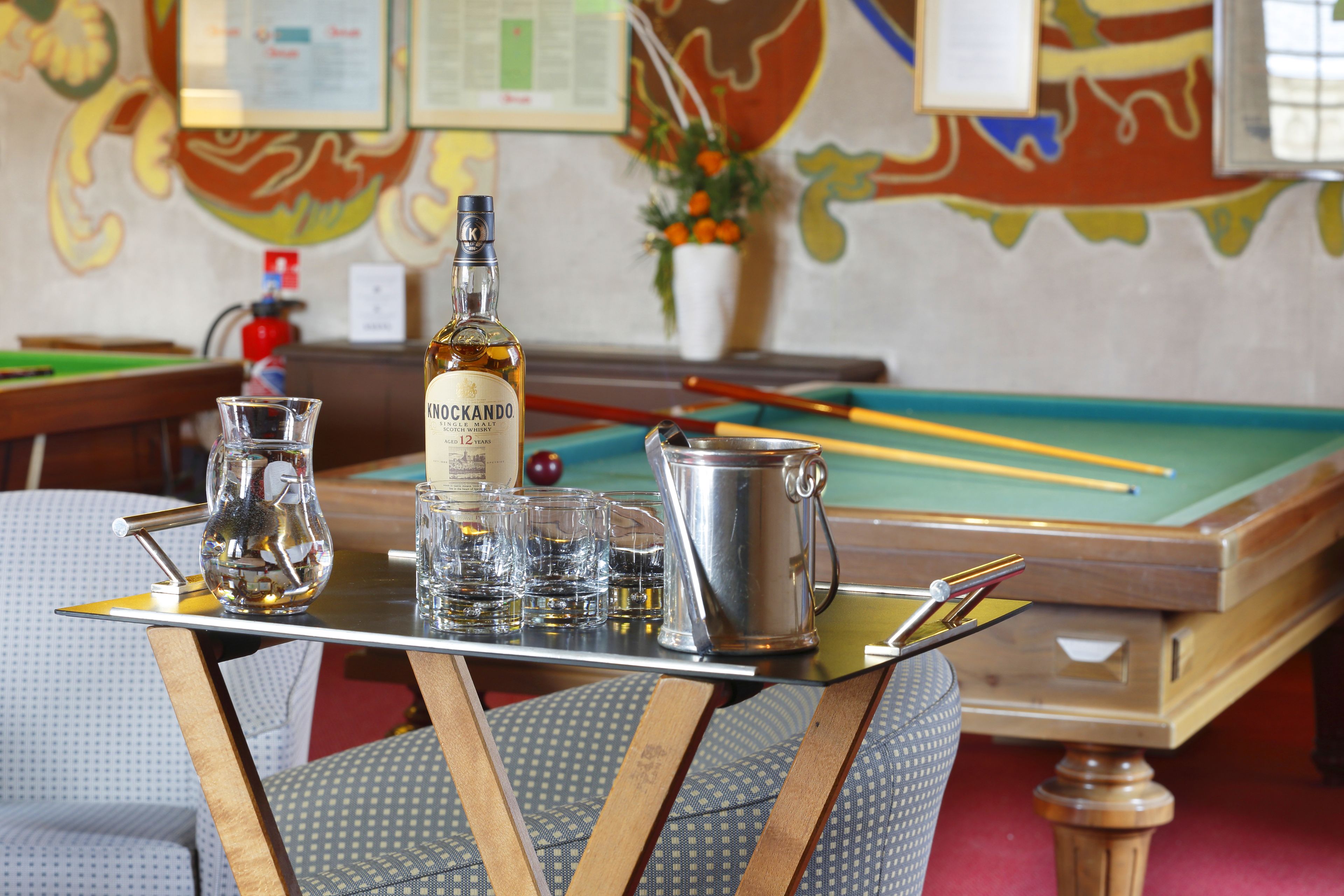 A pool table with billiard balls, a bottle of Knockingdown gin, and a glass pitcher.