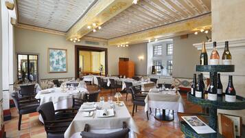A restaurant with multiple tables set for dining, a wine display, and a large painting on the wall.