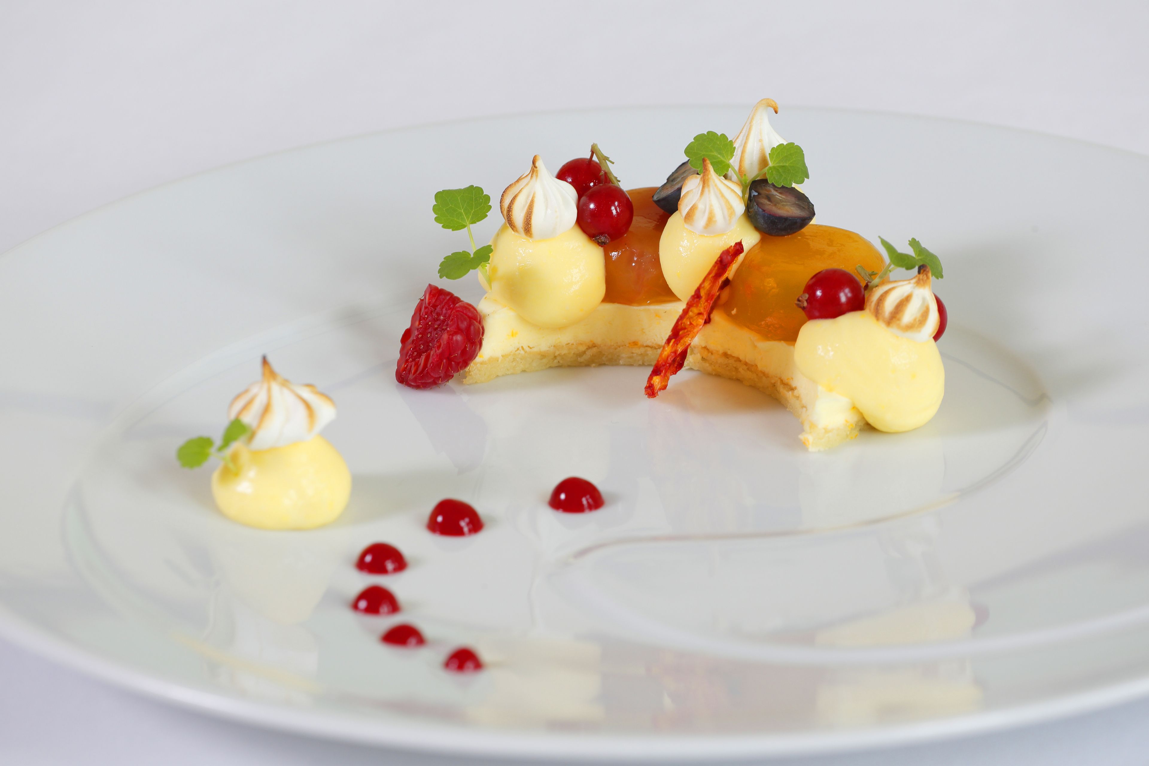 Un plato de postre con varias frutas y merengue sobre una vajilla blanca.