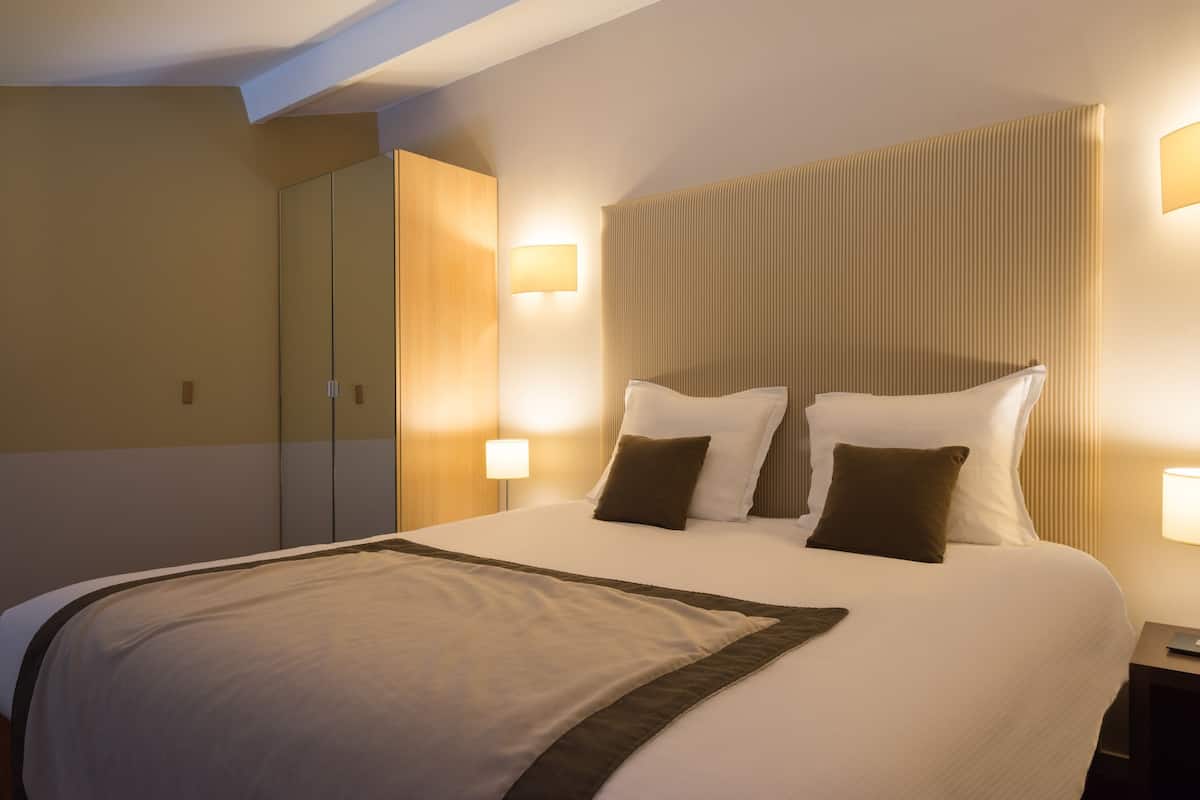 Una habitación de hotel con una cama grande, lámparas de noche, un armario y un espejo.