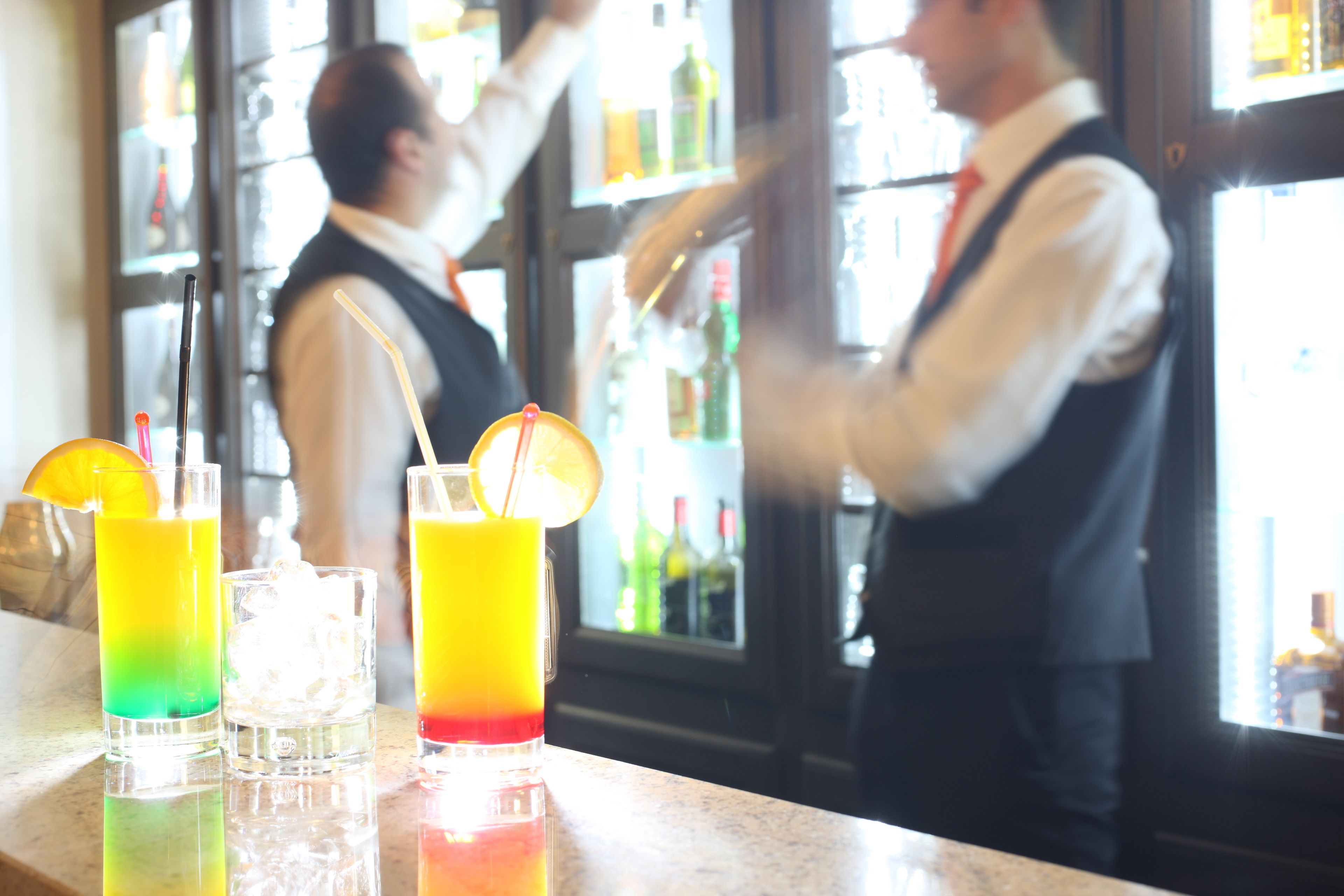 Un bar con dos cantineros preparando bebidas.