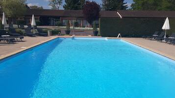 Una piscina rectangular con agua azul cristalina, rodeada de sillas de descanso y sombrillas.