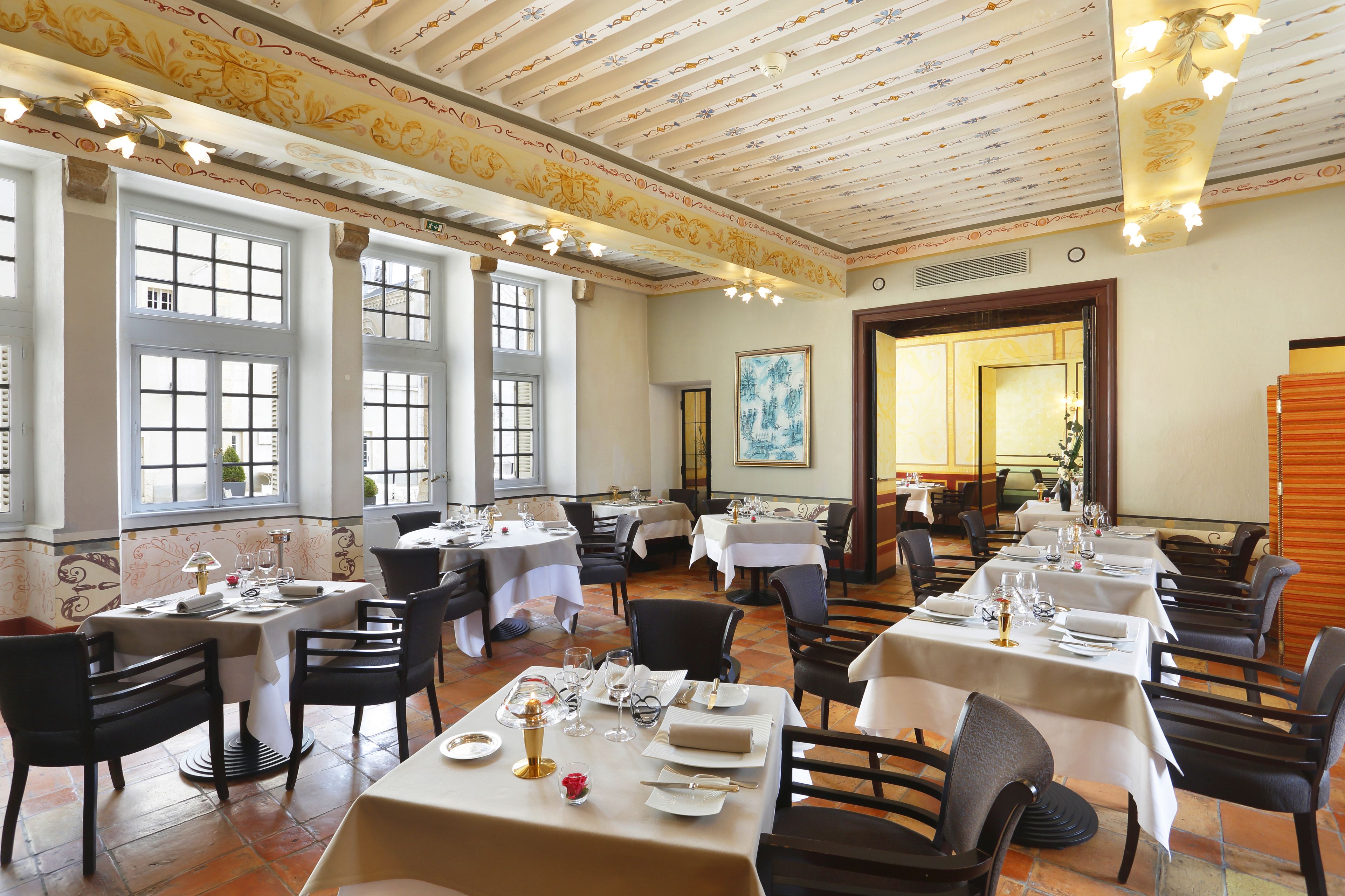 Un comedor con varias mesas listas para el servicio, ventanas amplias y un techo decorativo.