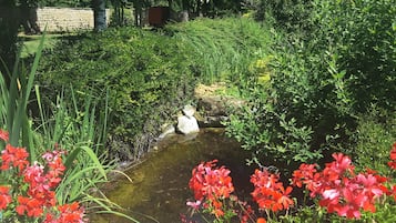 Un jardín con un pequeño arroyo, abundante vegetación y plantas en flor.