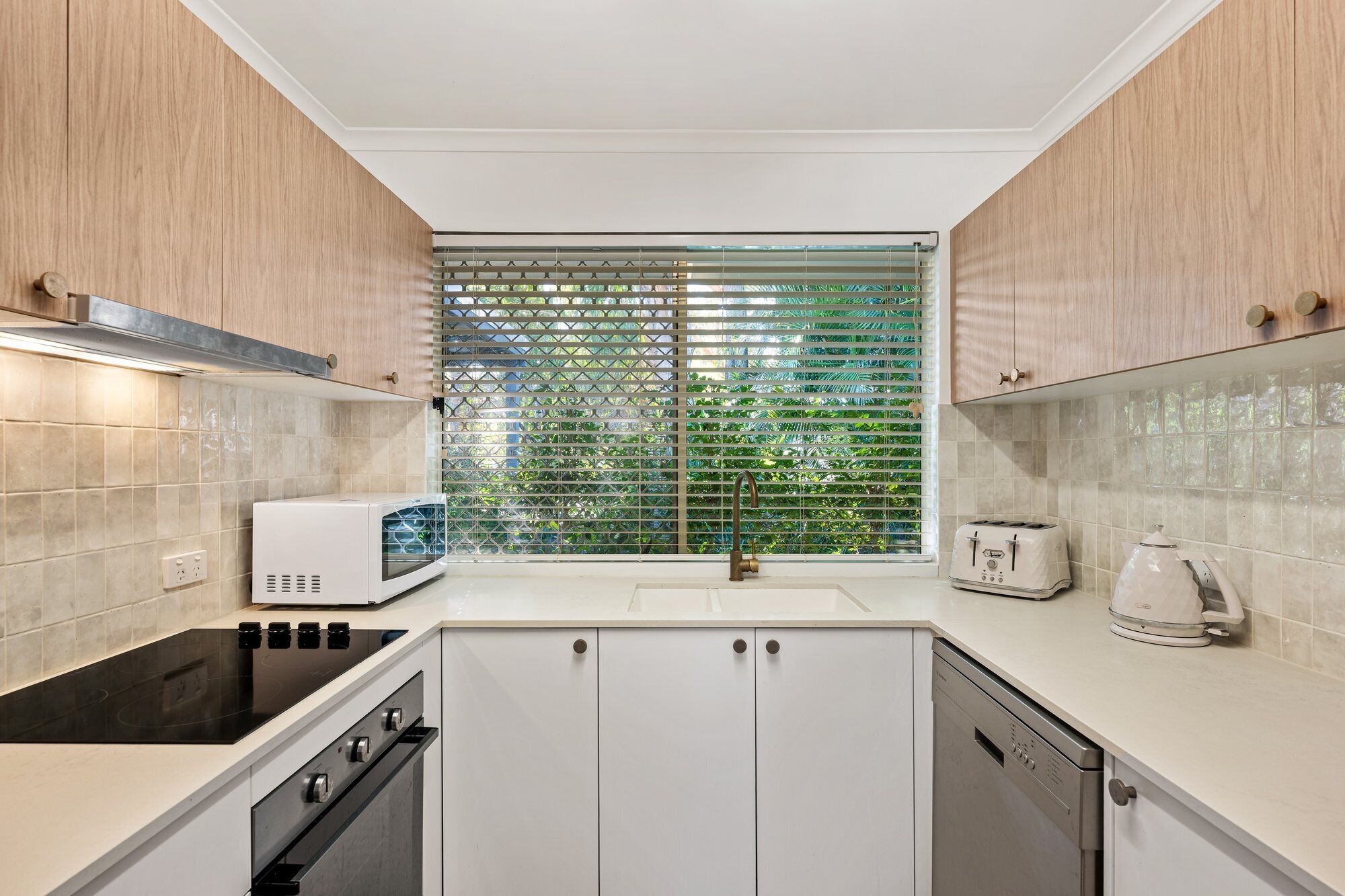 A modern kitchen with a built-in stove, oven, and dishwasher, a window with a view of greenery, and a toaster on the counter.