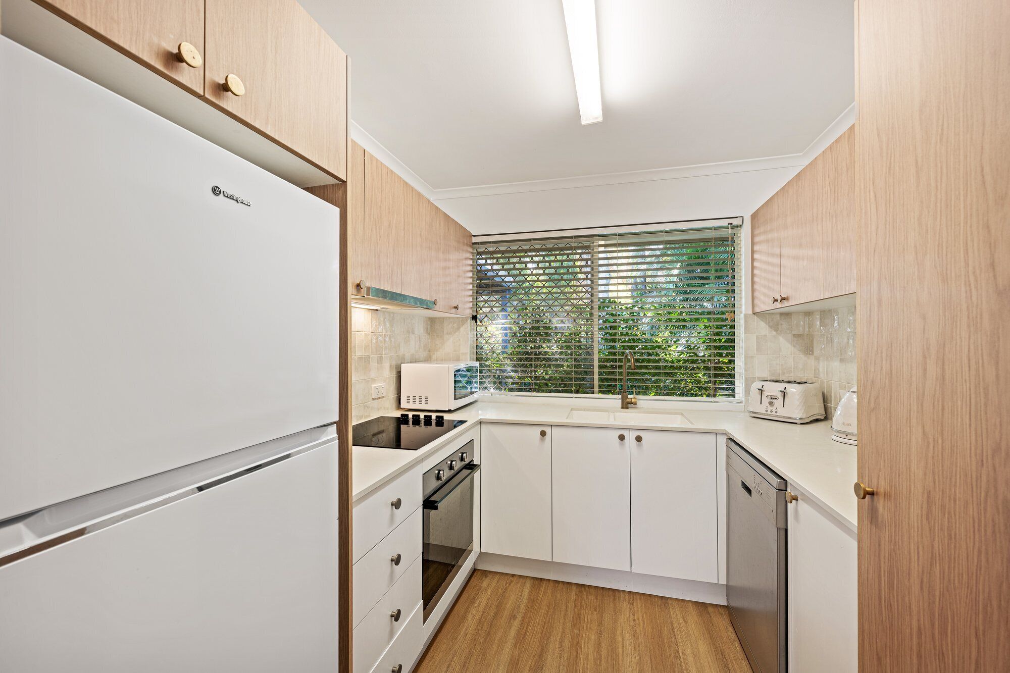 Una cocina compacta con armarios blancos, horno integrado, microondas y tostadora.