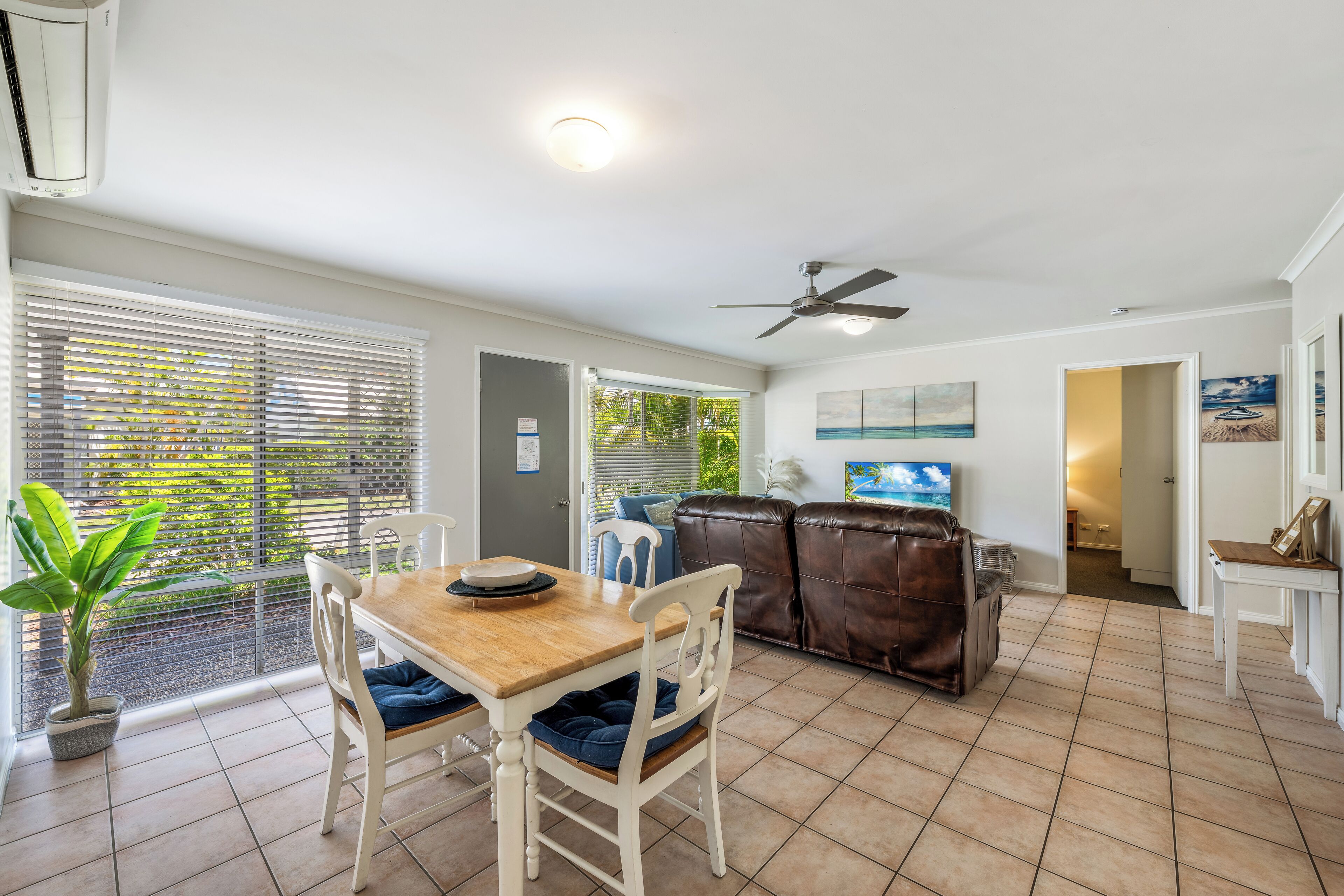 Un vaste espace de vie comprenant une table à manger, des chaises, un canapé en cuir et un ventilateur de plafond.