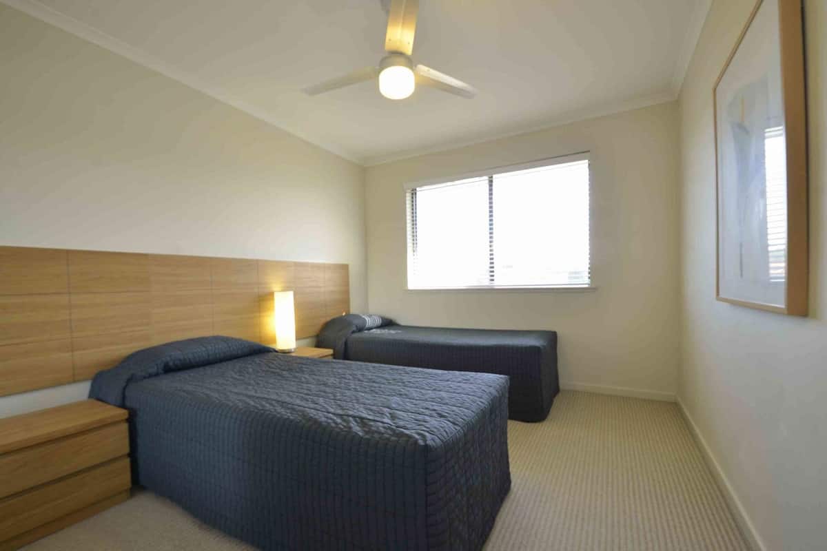 A bedroom with a bed, bedside table, lamp, and a window with blinds.