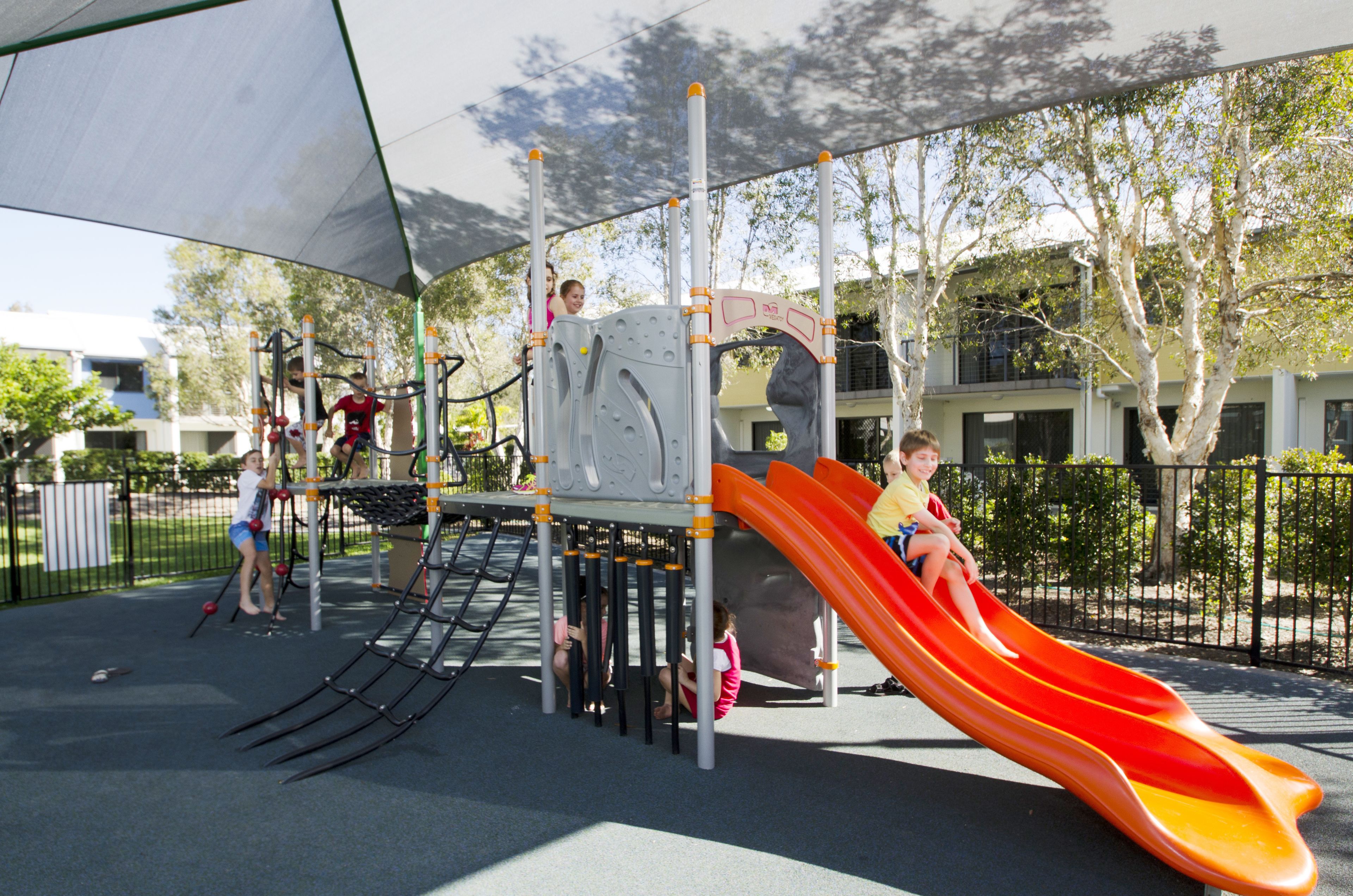 A playground with a slide, climbing structures, and a shaded area.