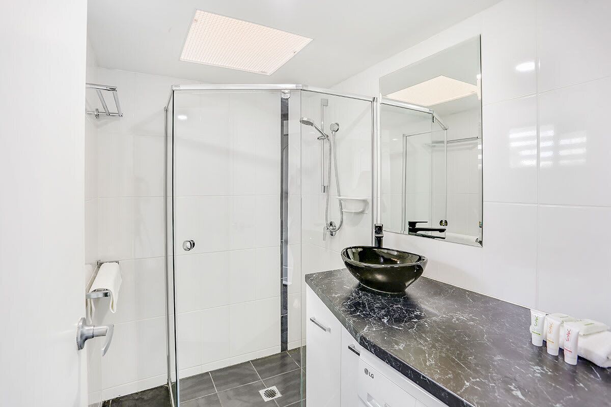 A modern bathroom with a glass shower enclosure, a black marble sink, and a large mirror.