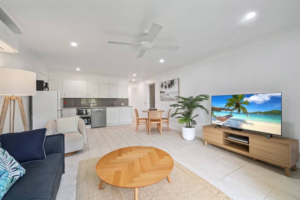 A modern living room with a sofa, coffee table, TV, and a dining area with chairs and a table.