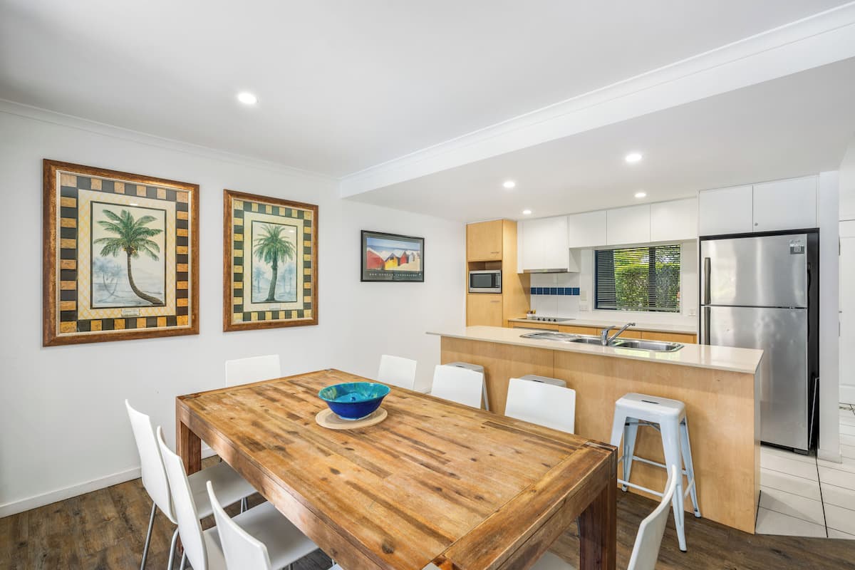 A modern kitchen with white cabinets, a stainless steel refrigerator, and a wooden dining table with a blue bowl.