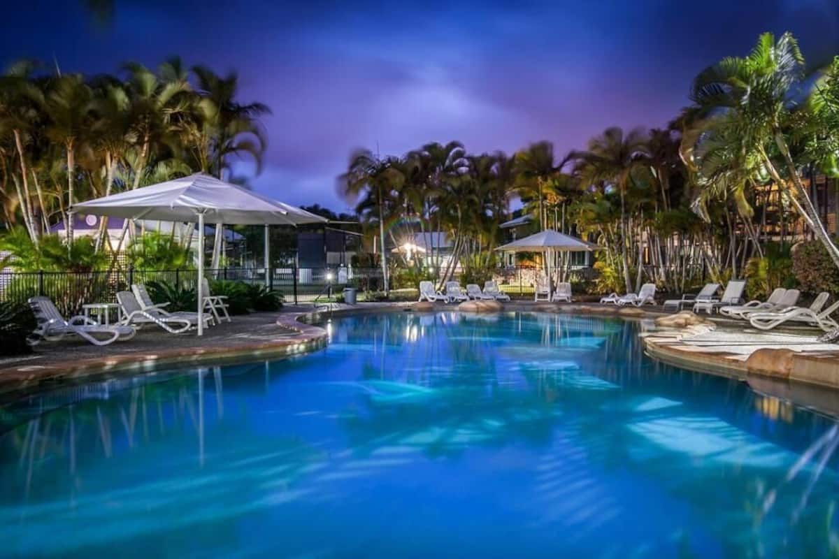 A swimming pool with lounge chairs and umbrellas, surrounded by palm trees.
