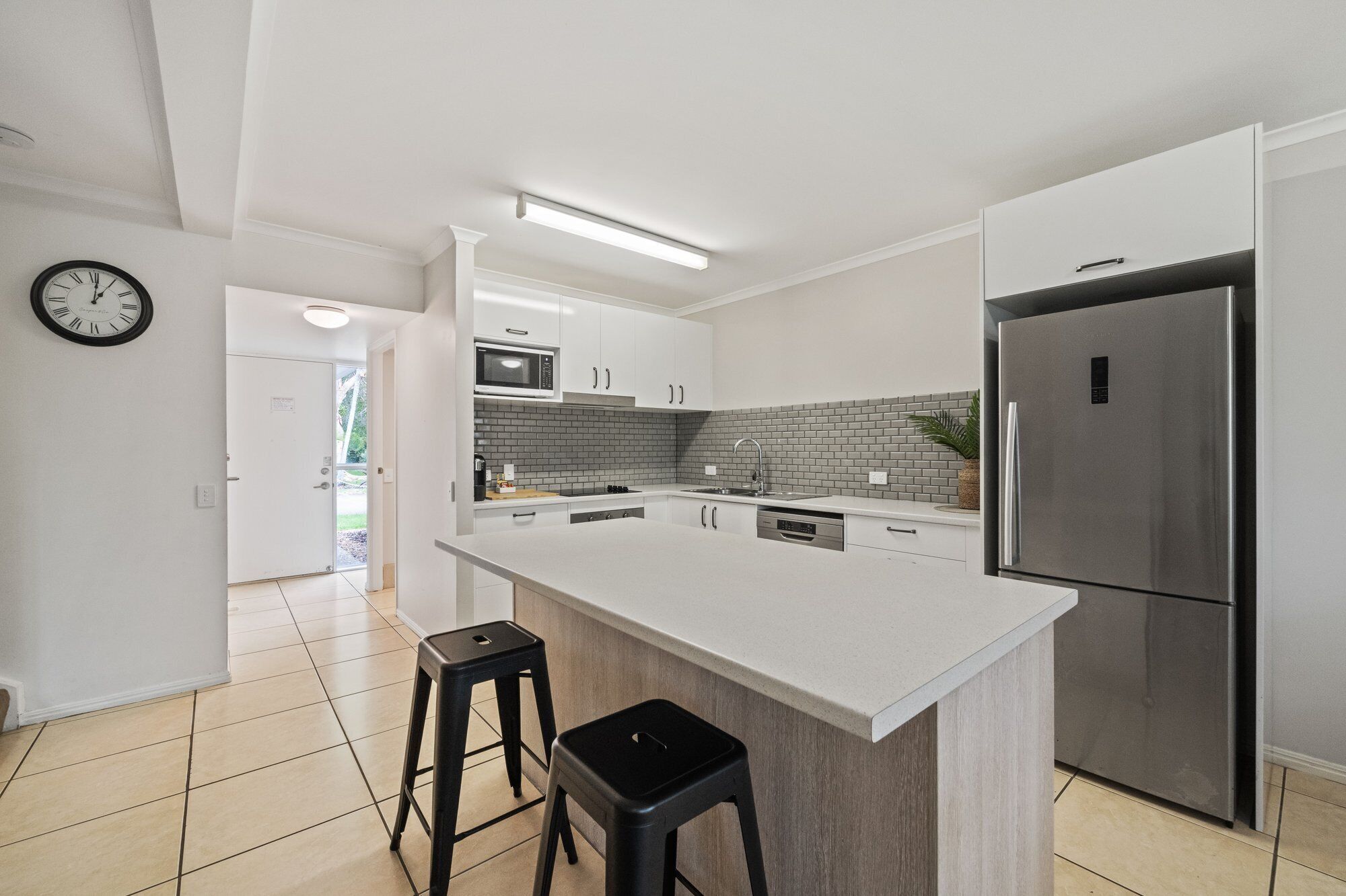 Una cocina moderna con armarios blancos, una isla grande, un refrigerador de acero inoxidable y un reloj en la pared.