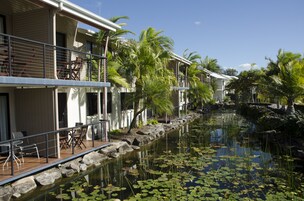 Um hotel com área de piscina, mobiliário de exterior e um elemento aquático com pedras e folhas de ninfeia.