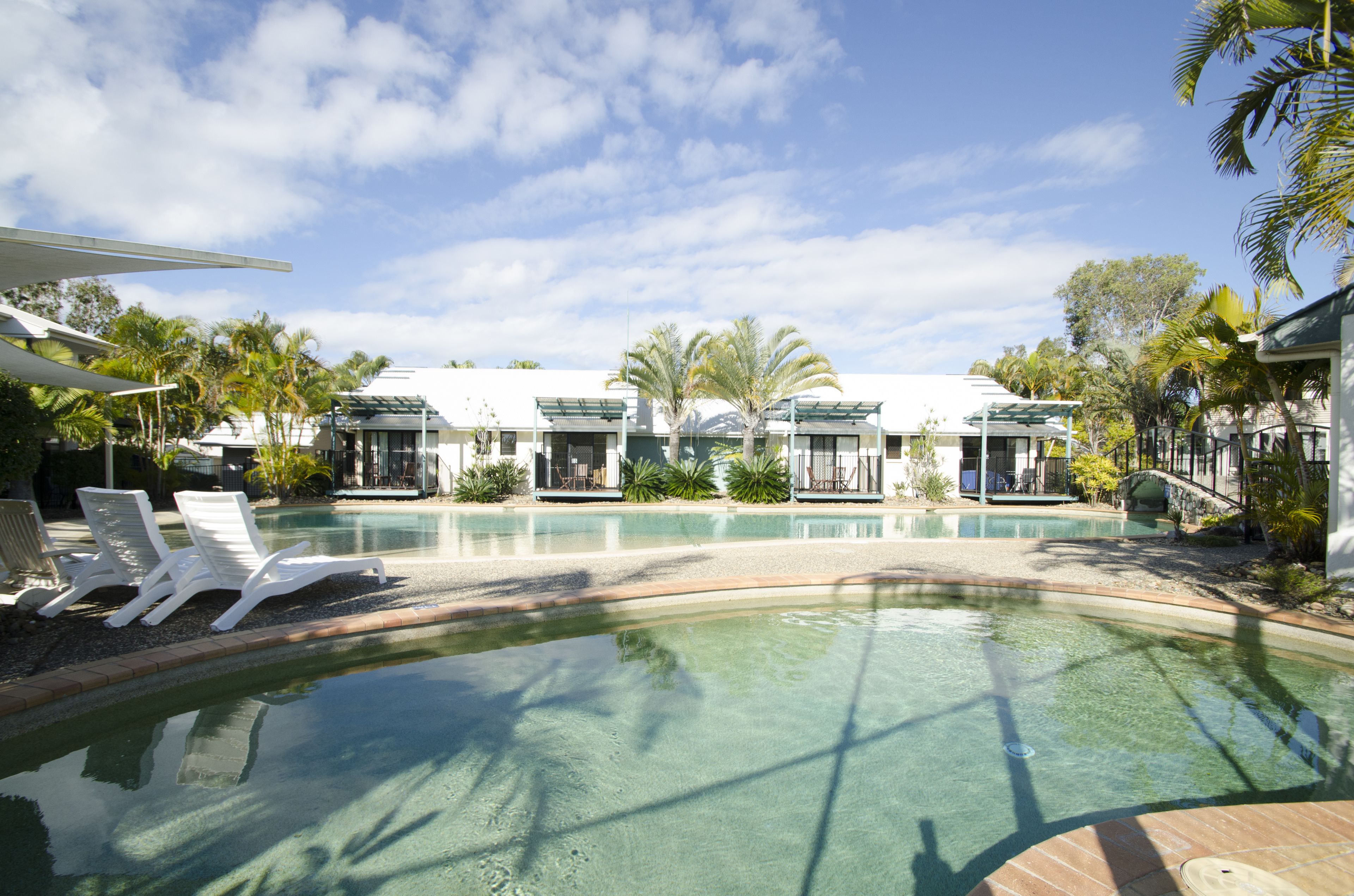 A pool area with lounge chairs, palm trees, and modern buildings with large windows.