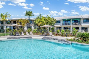 Um hotel com área de piscina, várias espreguiçadeiras e guarda-sóis.