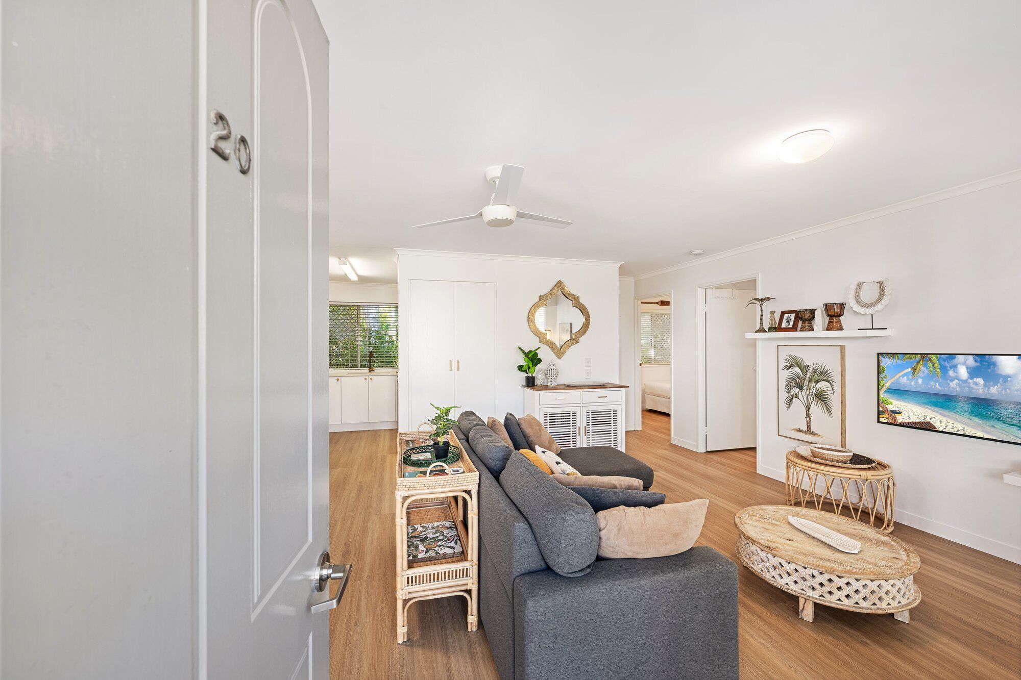 A living room with a grey sofa, wicker side table, and a ceiling fan.