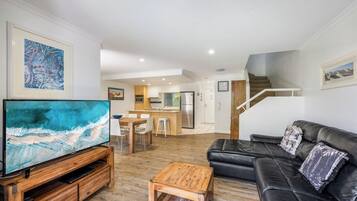 Una sala de estar moderna con un televisor de pantalla plana, una mesa de centro de madera, un sofá de cuero negro y una escalera que conduce a una zona de cocina.