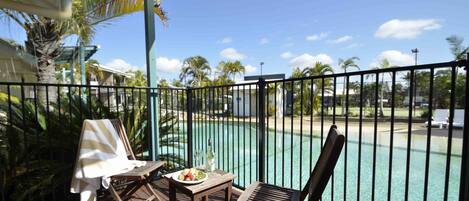 Ein Balkon mit Blick auf einen Pool, Holzmöbel und ein Tisch mit einer Fruchtschale und einer Flasche.