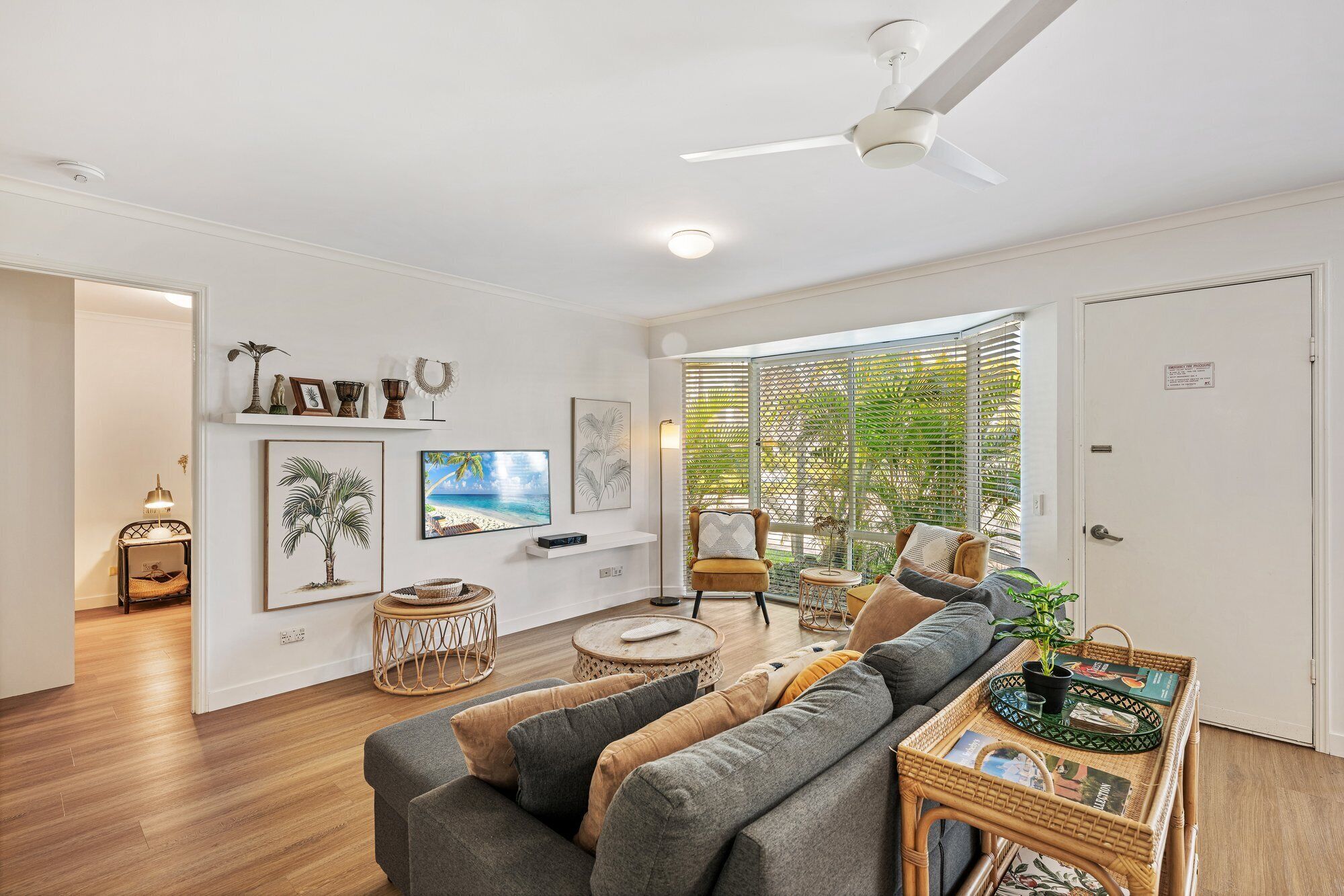 A living room with a sofa, a coffee table, a ceiling fan, and a large window with blinds.