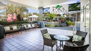 Un patio al aire libre con mobiliario de mimbre, una mesa de vidrio y un letrero que indica 'PR's Café & Bar'.