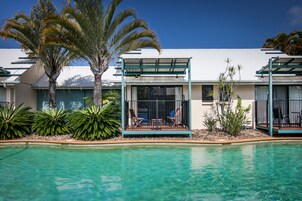 Um hotel com piscina, palmeiras e área de estar coberta ao ar livre.