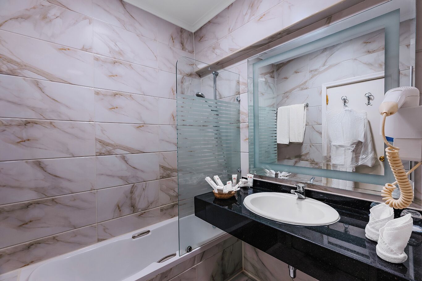 A bathroom with a marble wall, a glass shower enclosure, a black sink, and a towel rack.