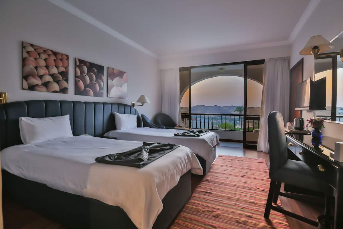 Habitación de hotel con dos camas, un escritorio y vistas a las montañas.