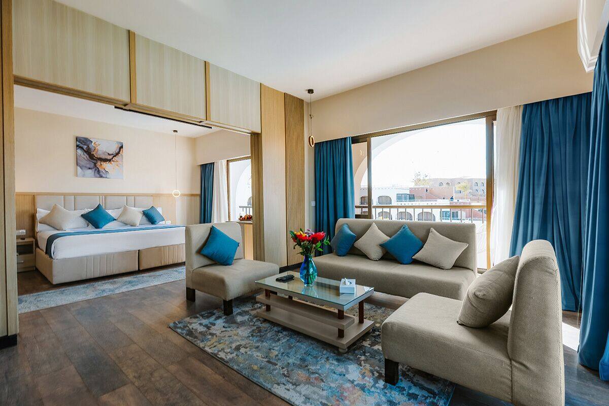Una habitación de hotel moderna con una cama, dos sofás, una mesa de centro y un ventanal con cortinas.