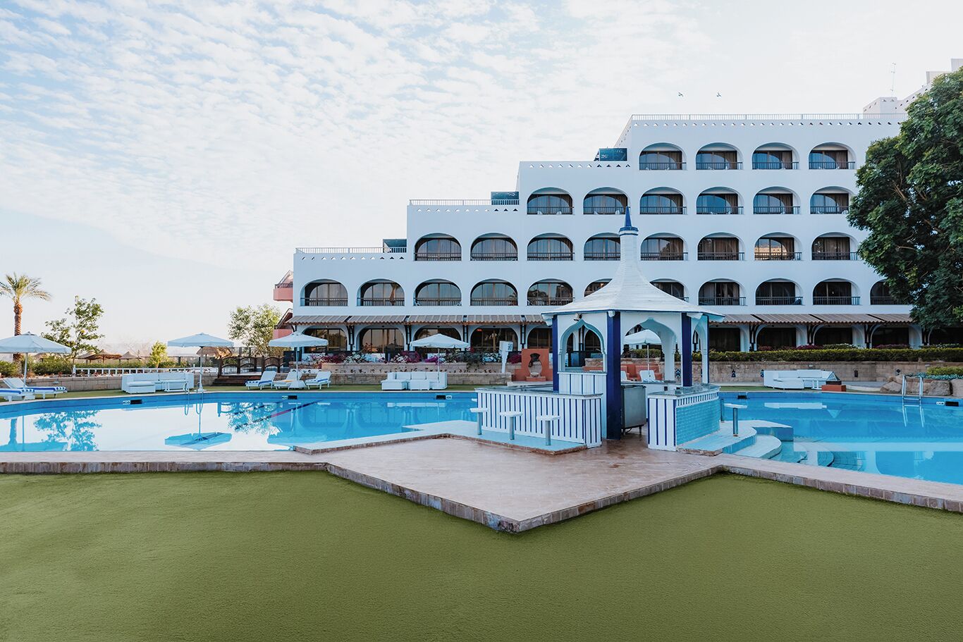 A hotel with a large pool area, multiple lounge chairs, and a gazebo.