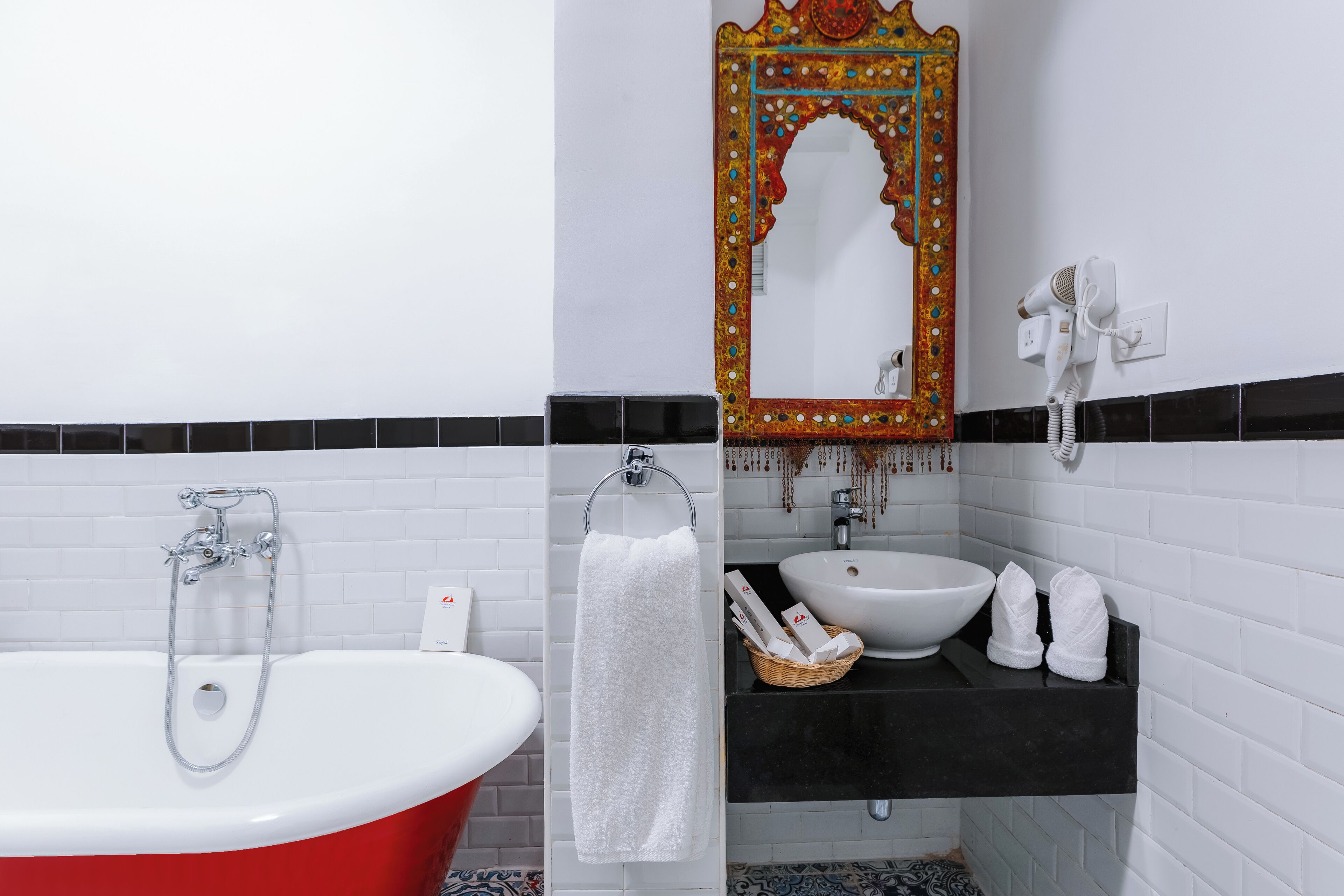 A bathroom with a red bathtub, white sink, and a decorative mirror.