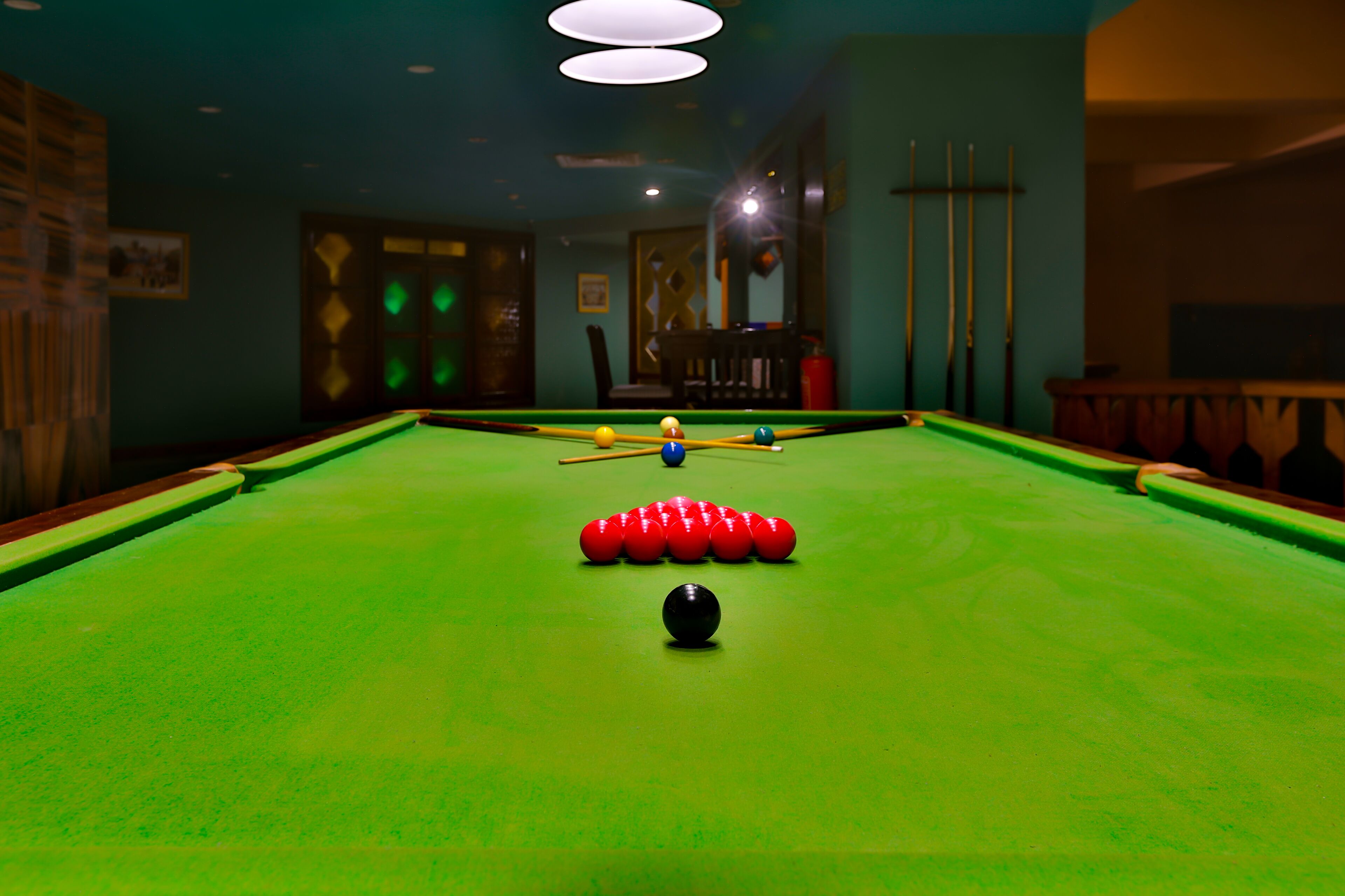 A pool table with balls and cues, surrounded by a room with teal walls and a wooden chair.