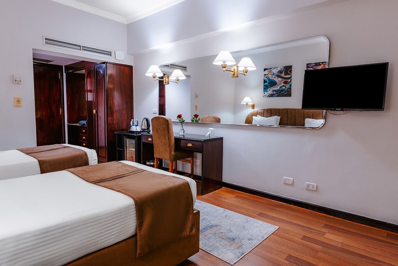 Une chambre d’hôtel avec deux lits, un bureau, une chaise, une télévision et un miroir.