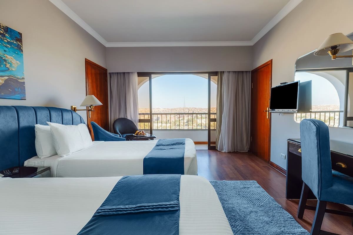 Habitación de hotel con dos camas, un escritorio, una silla, un televisor y vistas a la ciudad.