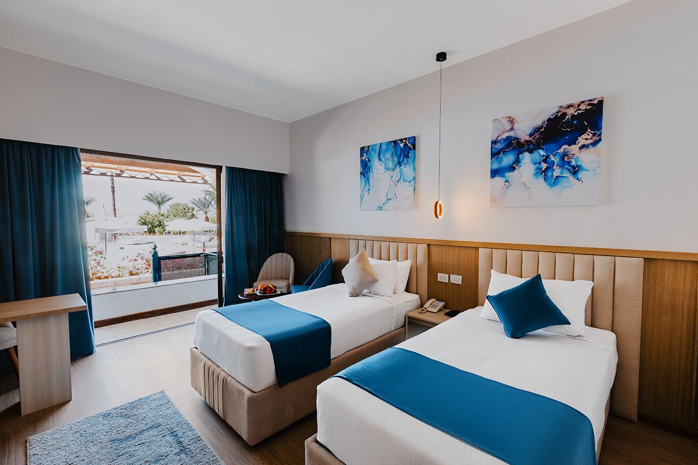 Habitación de hotel con dos camas, un escritorio y vistas al exterior.