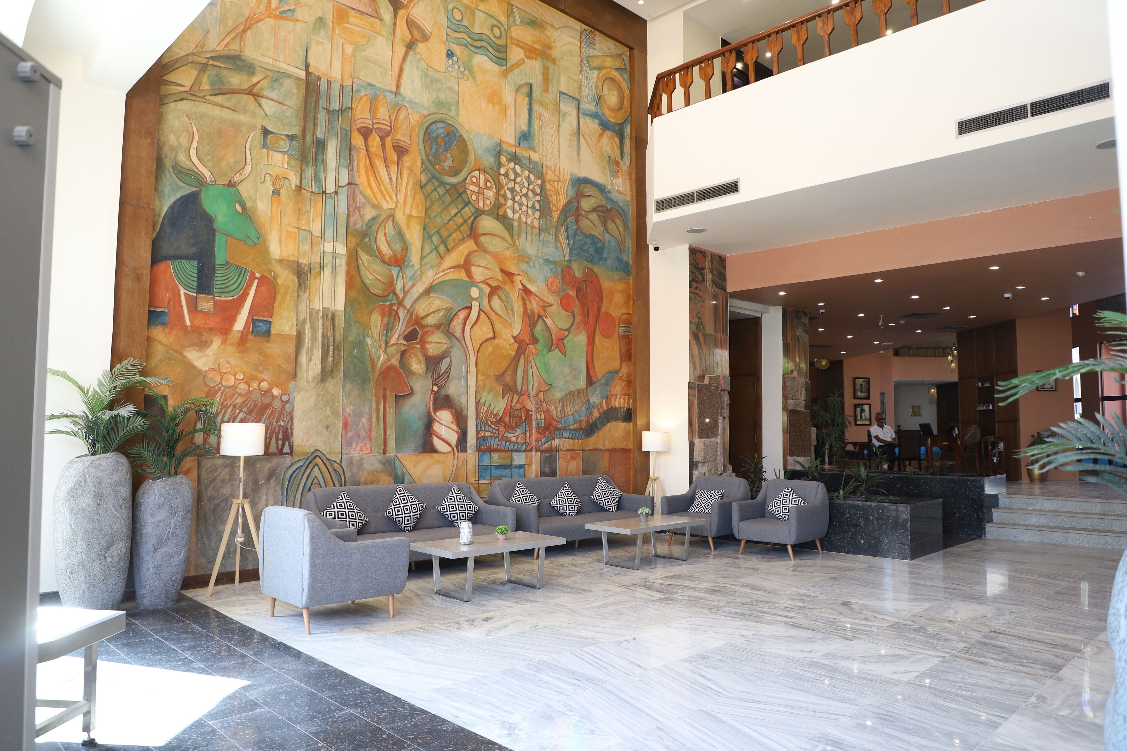 A spacious lobby with a large abstract mural, seating area with sofas and tables, and a staircase leading to an upper level.