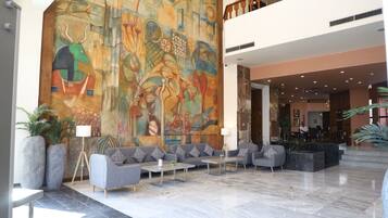 A spacious lobby with a large abstract mural, seating area with sofas and tables, and a staircase leading to an upper level.