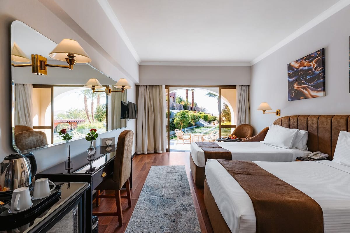 Habitación de hotel con cama, escritorio, silla, cafetera y vistas al exterior.