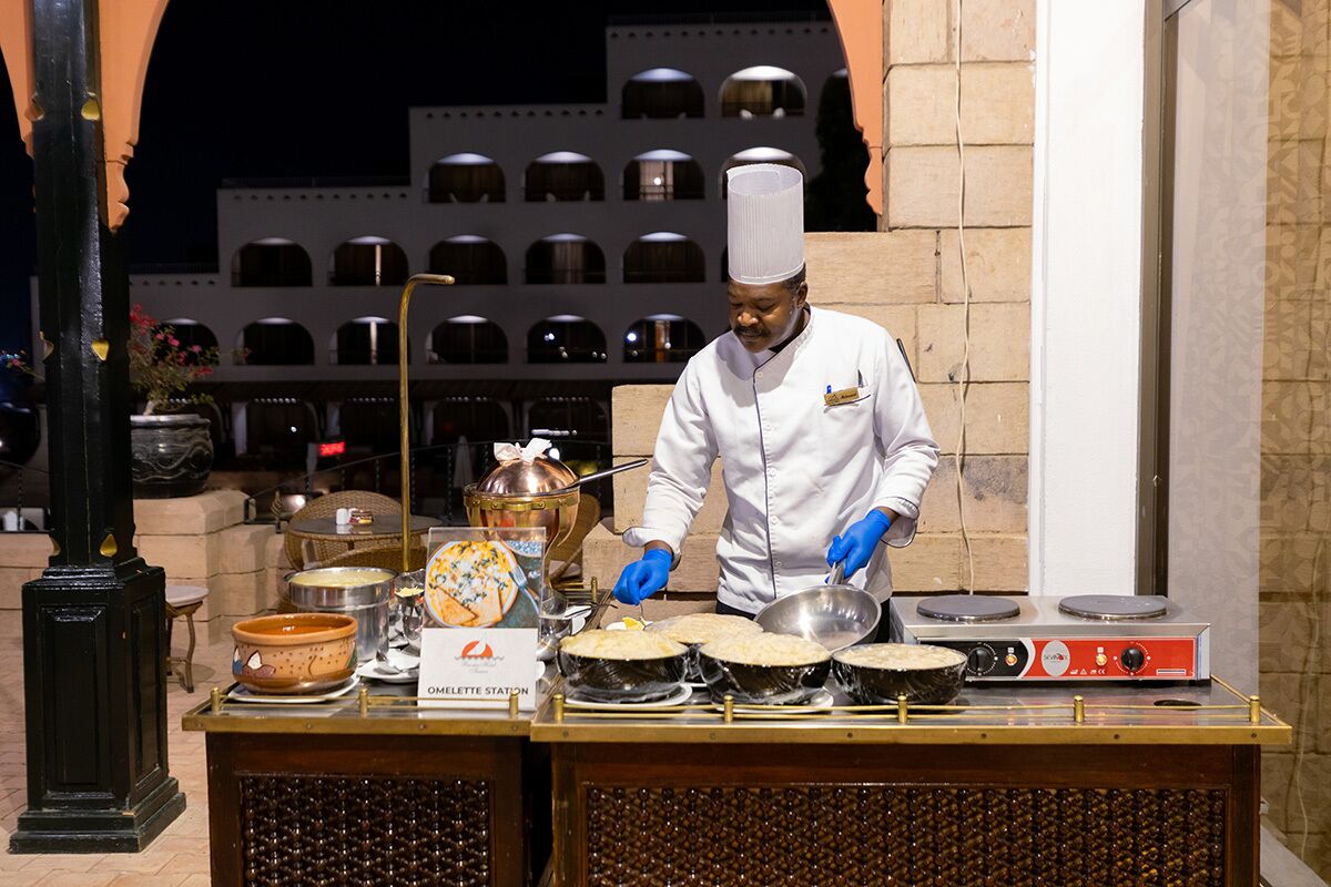 A chef preparing food at an outdoor station with multiple cooking stations and a variety of cooking utensils and ingredients.