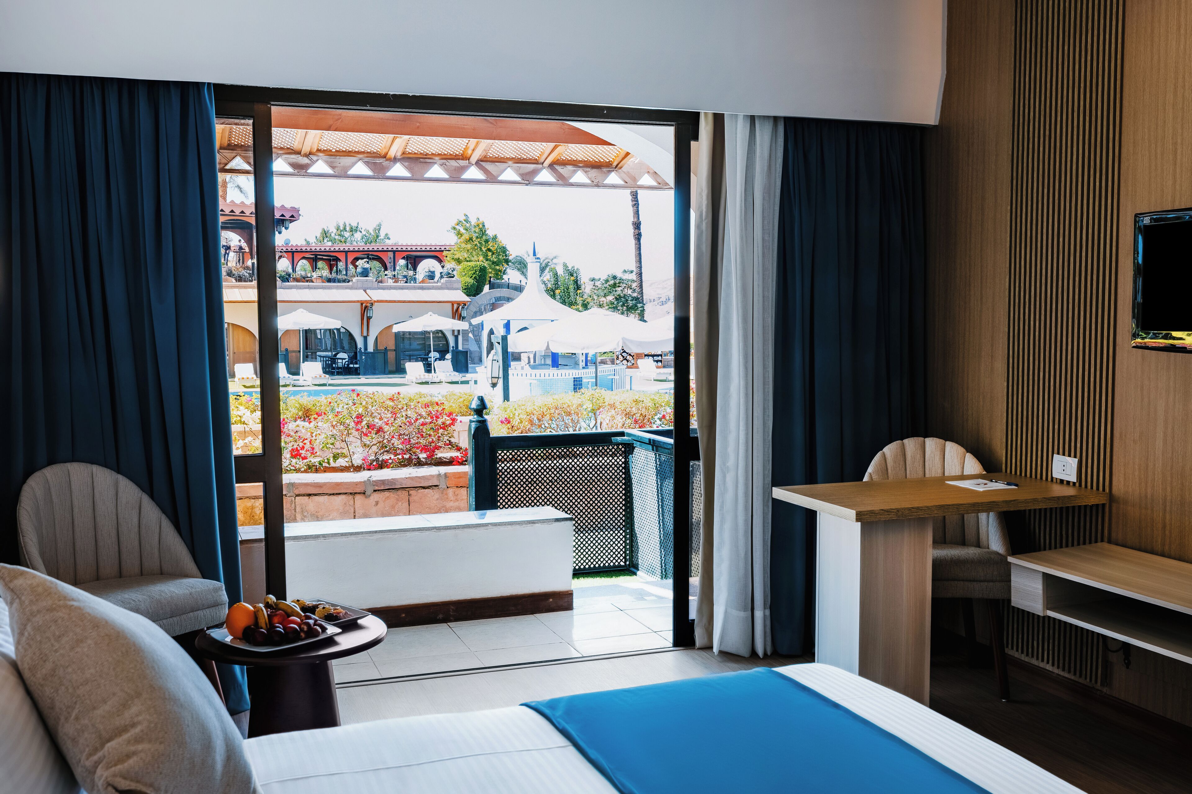 A hotel room with a bed, a desk, and a view of an outdoor pool area.