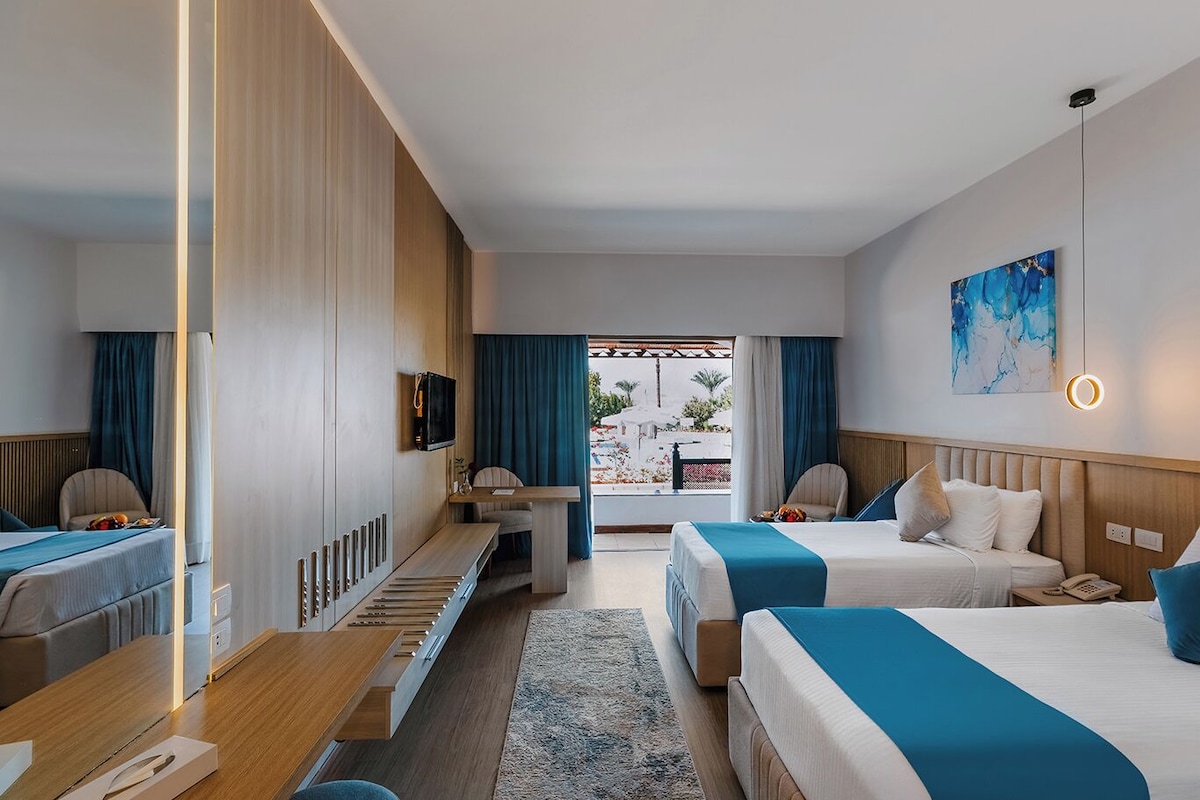 Habitación de hotel con dos camas, un escritorio, un televisor y vistas al exterior.