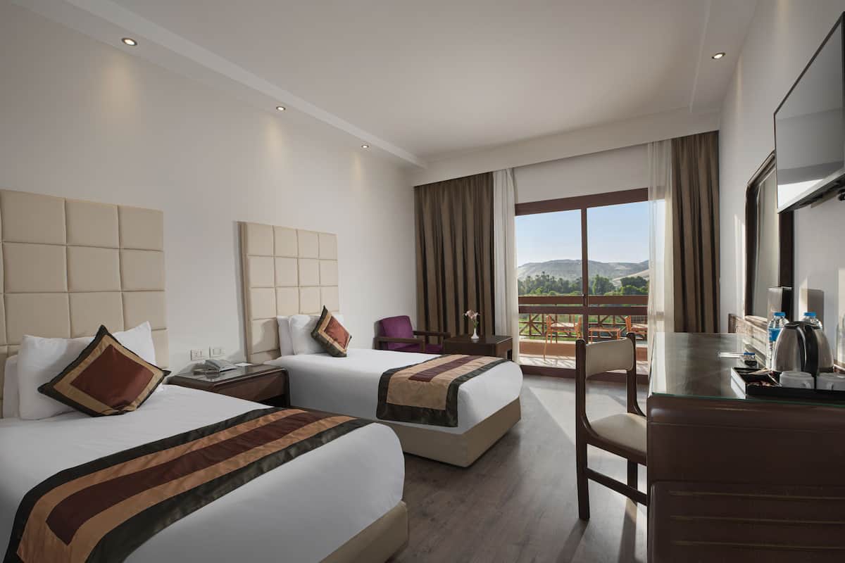 A hotel room with two beds, a desk, and a balcony with a view.